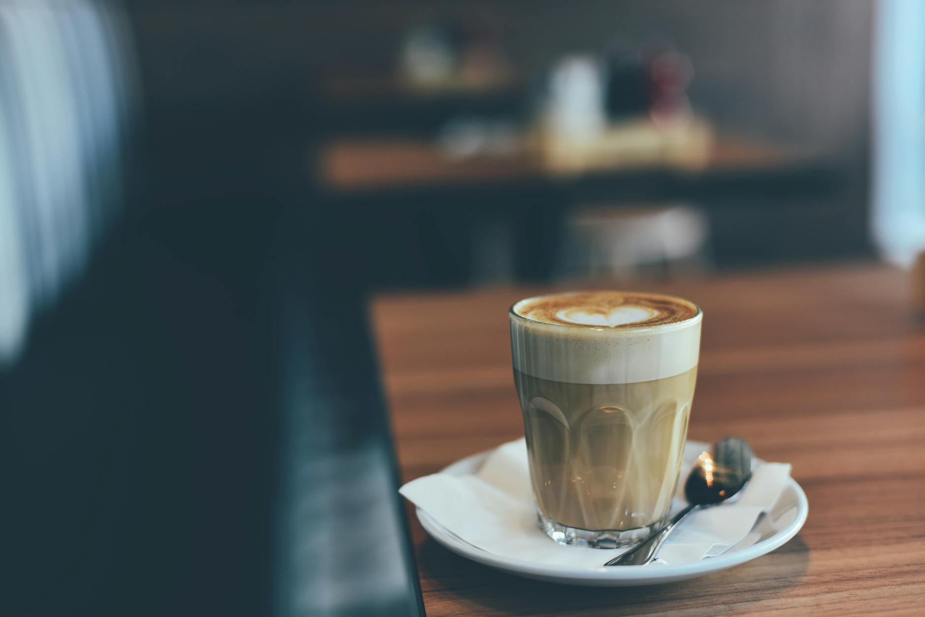 clear drinking glass with brown beverage in white saucer in tilt shift photography