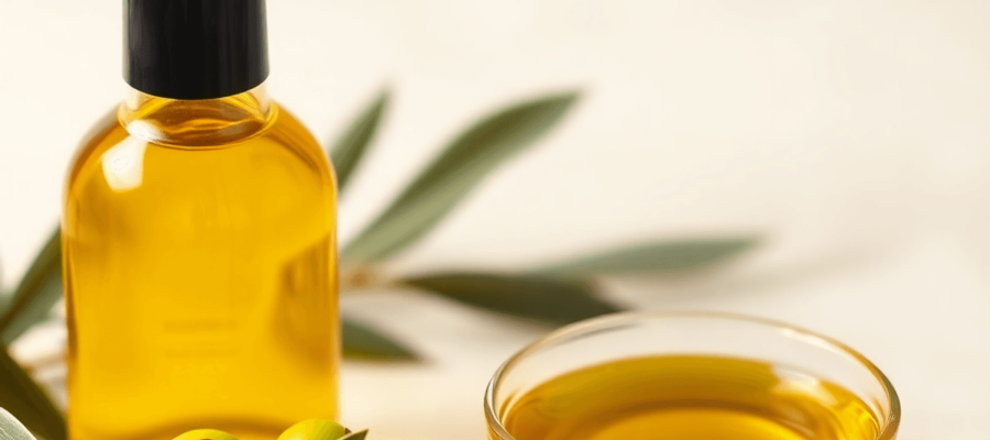 A close-up of a golden olive oil bottle, fresh green olives, and a small bowl of olive oil on a soft, neutral background, emphasizing natural beauty and wellness.