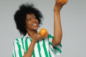 photo of smiling woman in white and green stripe shirt holding up orange fruits