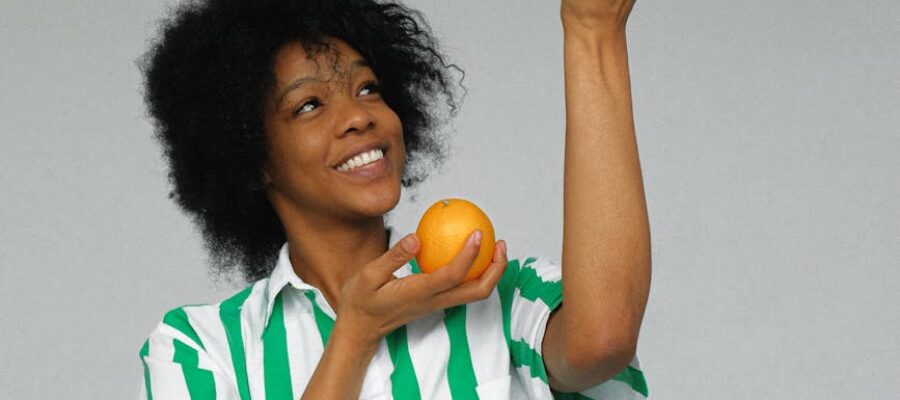 photo of smiling woman in white and green stripe shirt holding up orange fruits