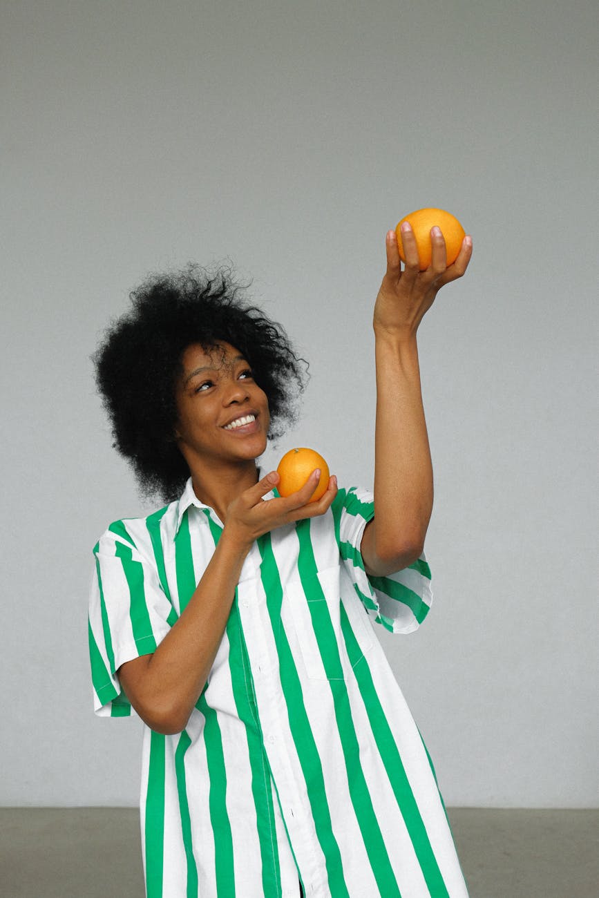 photo of smiling woman in white and green stripe shirt holding up orange fruits